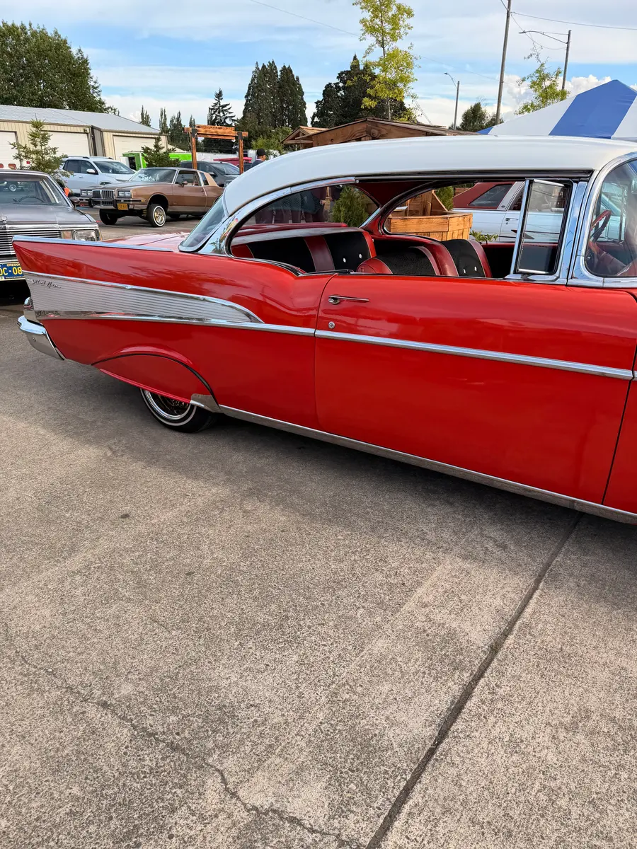 A red classic car with a white roof and chrome trim, with more cars parked behind it